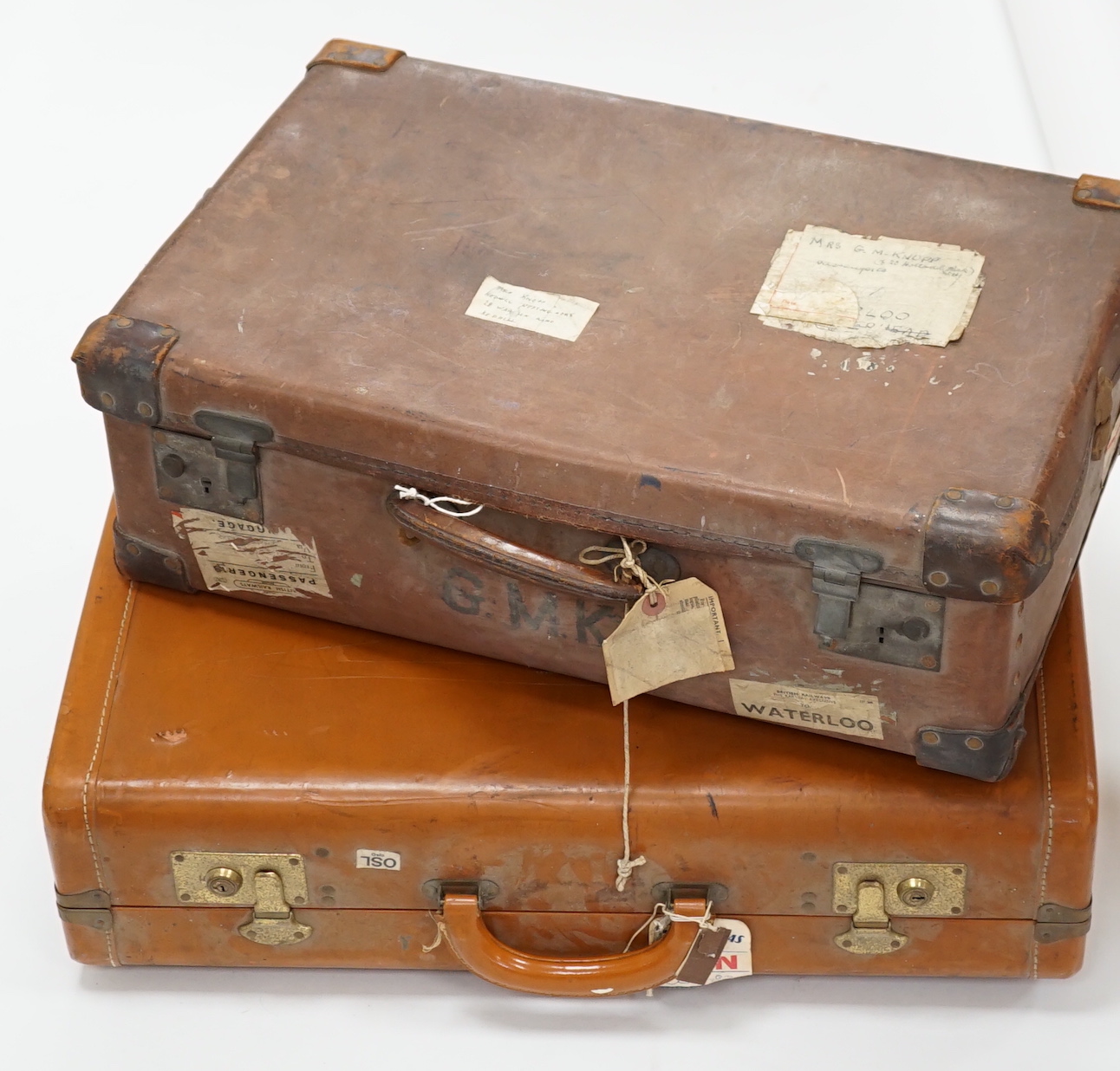 Two vintage suitcases with various labels including British Railways Waterloo, the largest 61cm wide